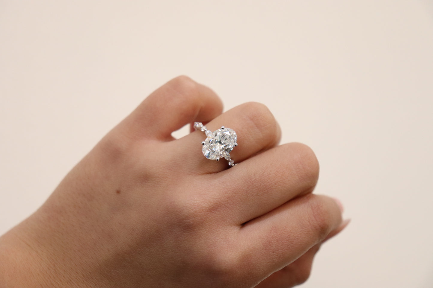 Hand wearing an Oval engagement ring with marquise and round accent band
