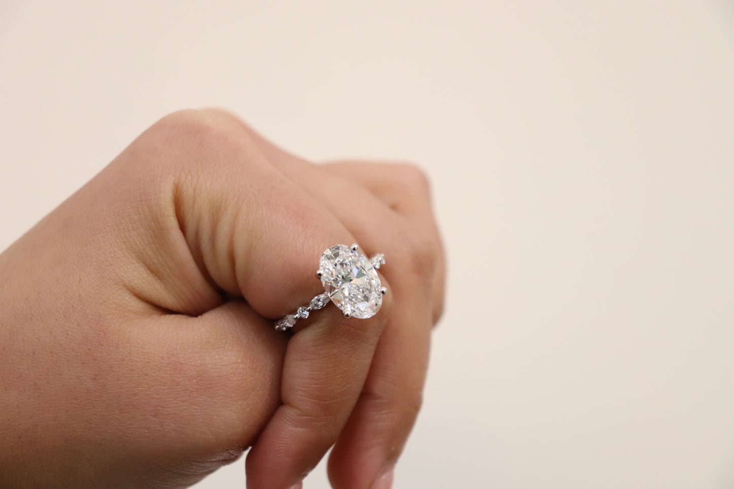 Hand wearing an Oval engagement ring with marquise and round accent band