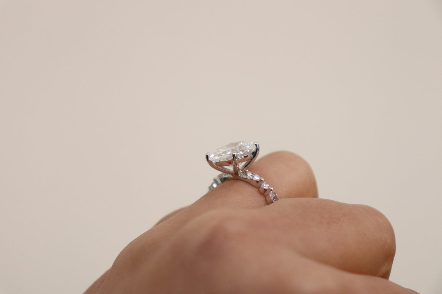 Hand wearing an Oval engagement ring with marquise and round accent band