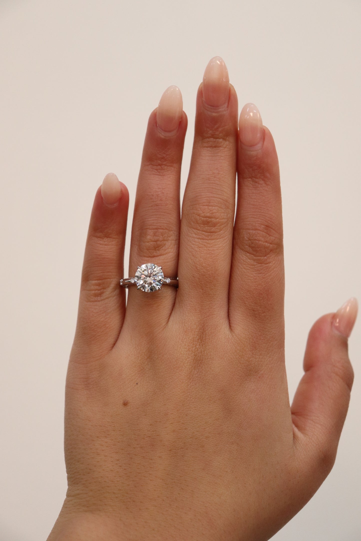 Hand wearing a round brilliant cut diamond ring on a plain background