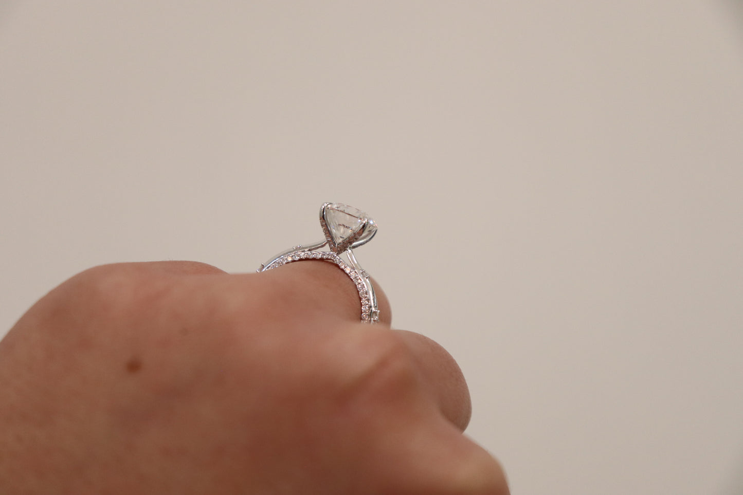 Diamond ring on a finger against a neutral background