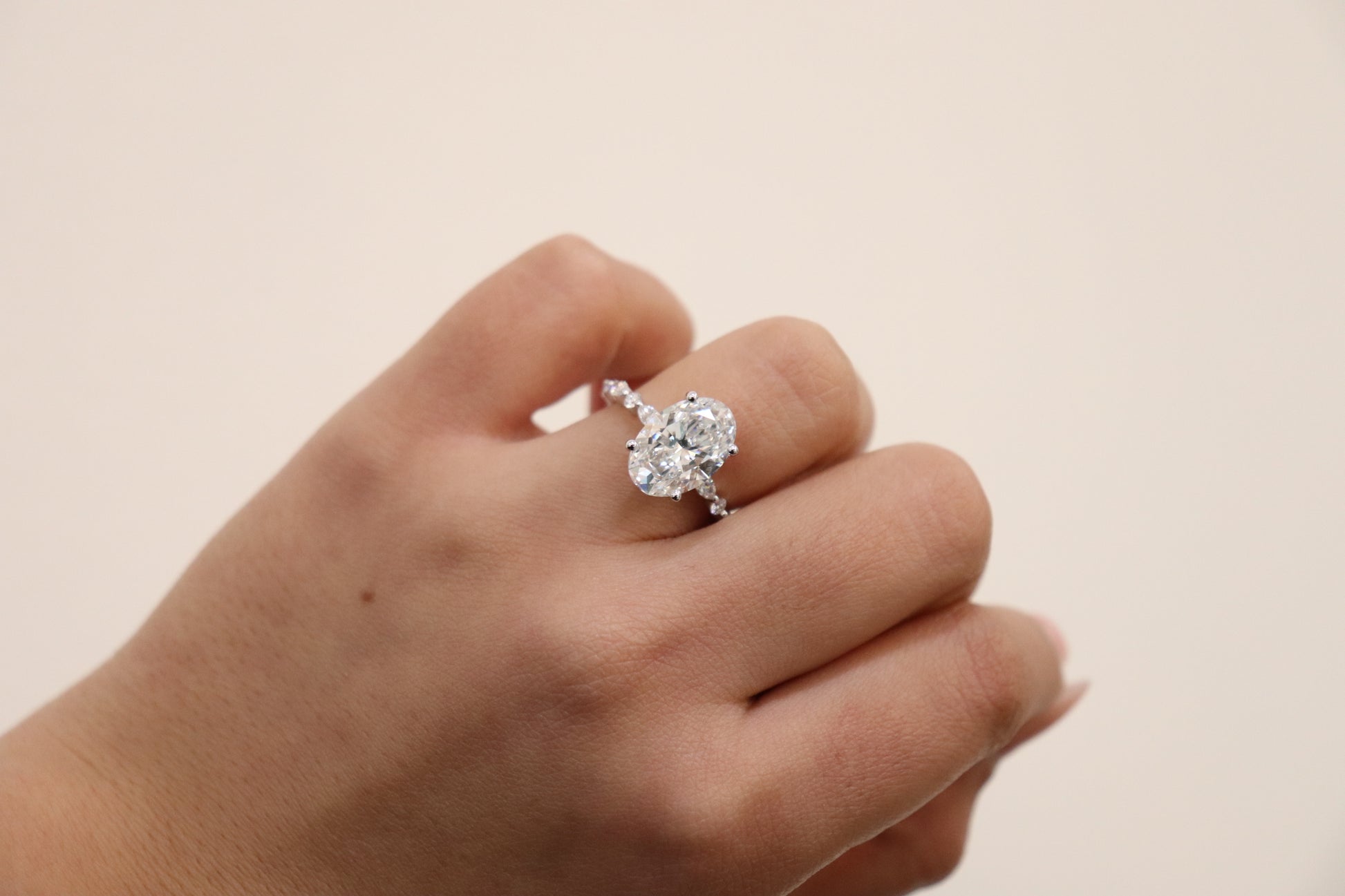 Hand wearing an Oval engagement ring with marquise and round accent band