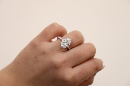 Hand wearing an Oval engagement ring with marquise and round accent band