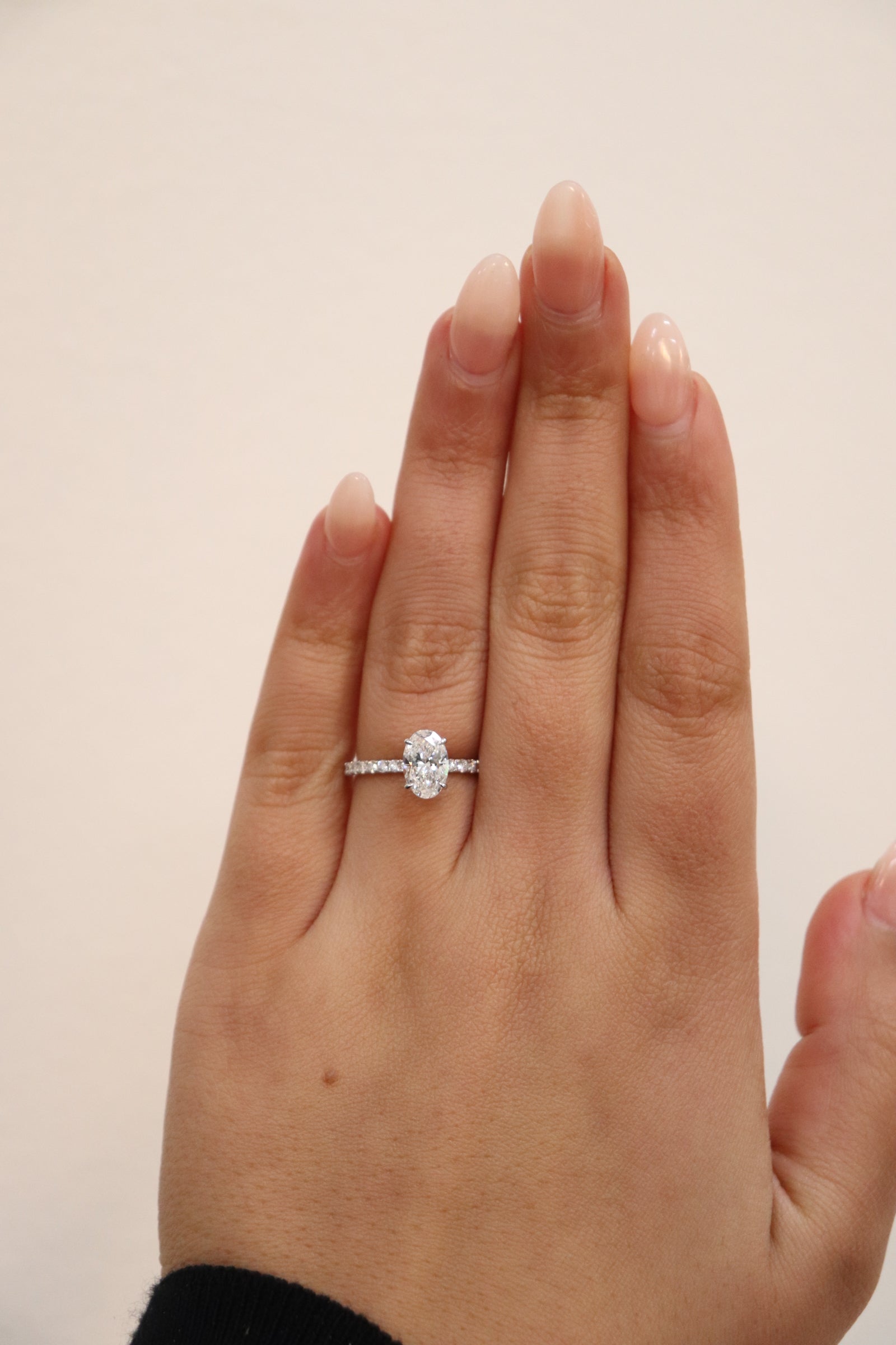 Hand wearing an oval cut diamond ring with pavè band on a plain background
