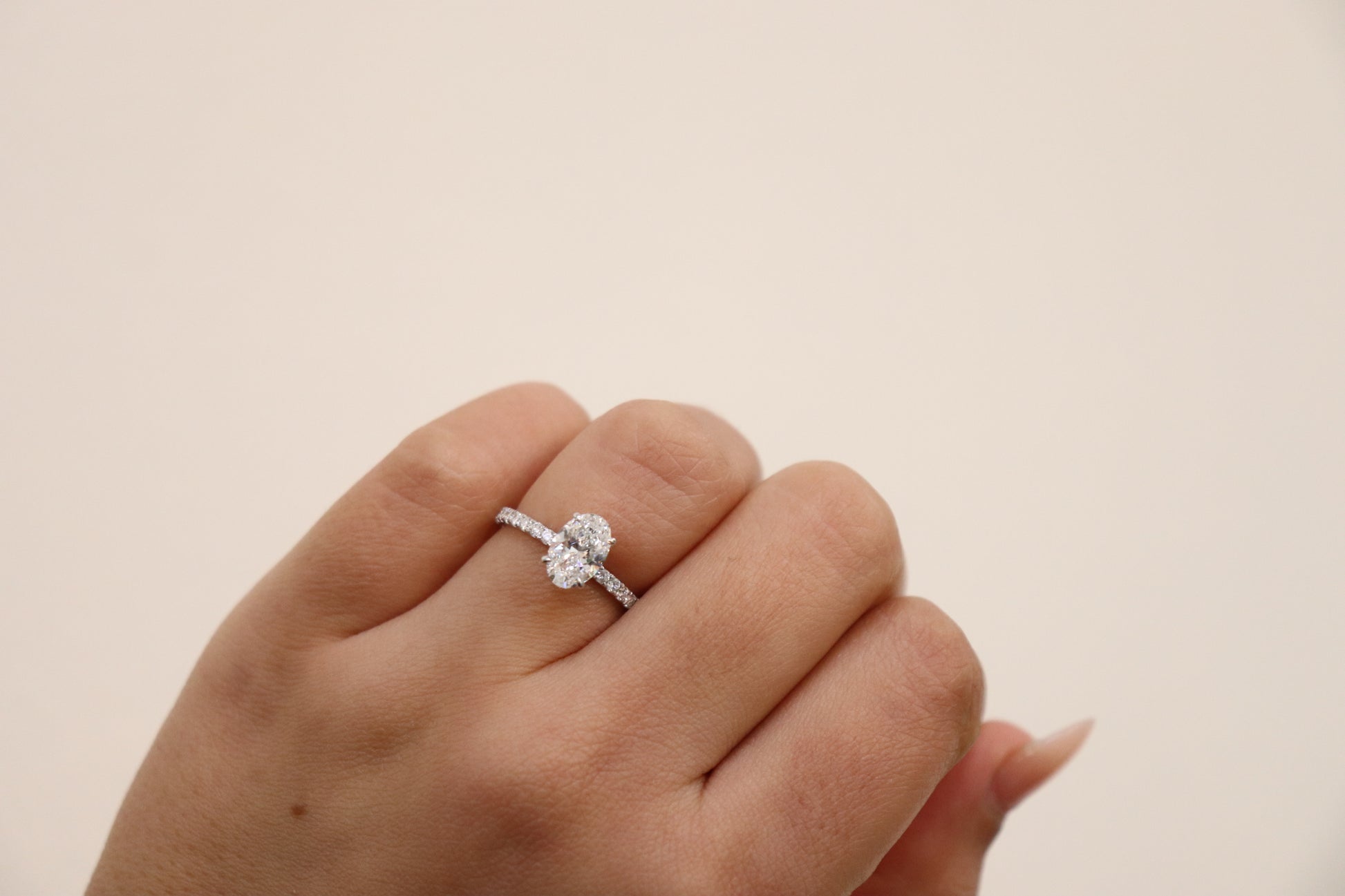 Hand wearing an oval cut  diamond ring on a beige background