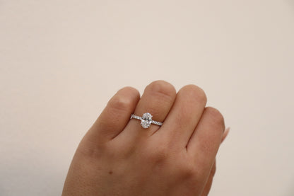 Hand wearing an oval cut diamond ring on a plain background