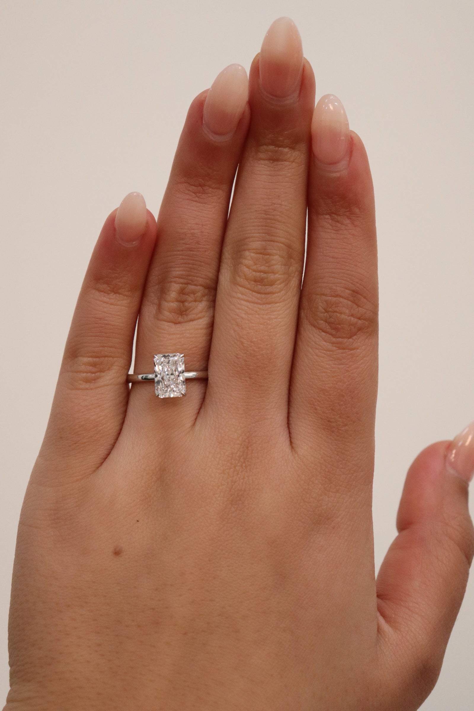 Hand wearing a Radiant cut diamond ring on a plain background