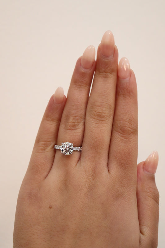 Hand wearing a Round Brilliant cut diamond ring with a pavè band on a plain background