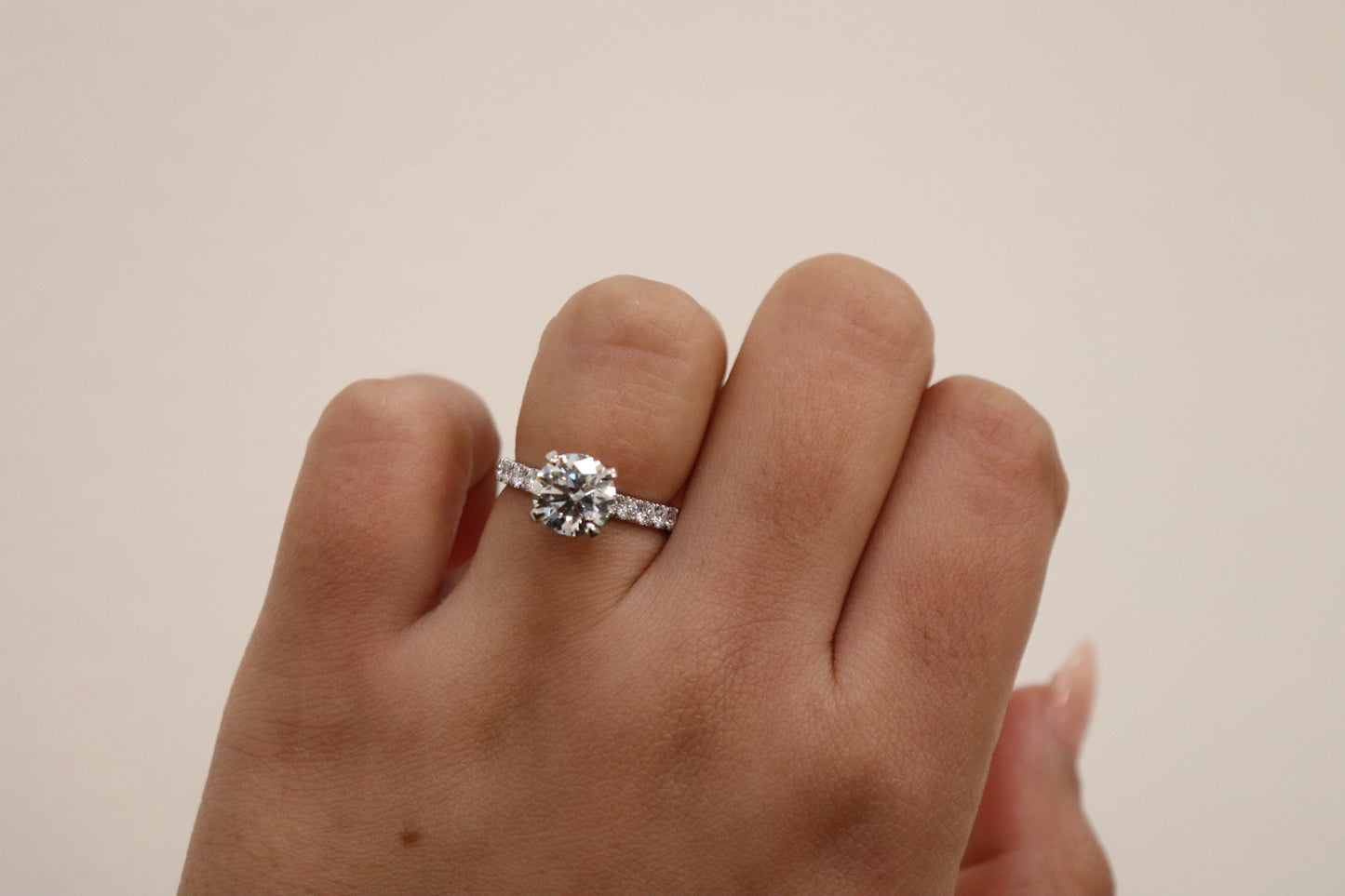 Round brilliant Cut Diamond with pavè band on a finger against a plain background