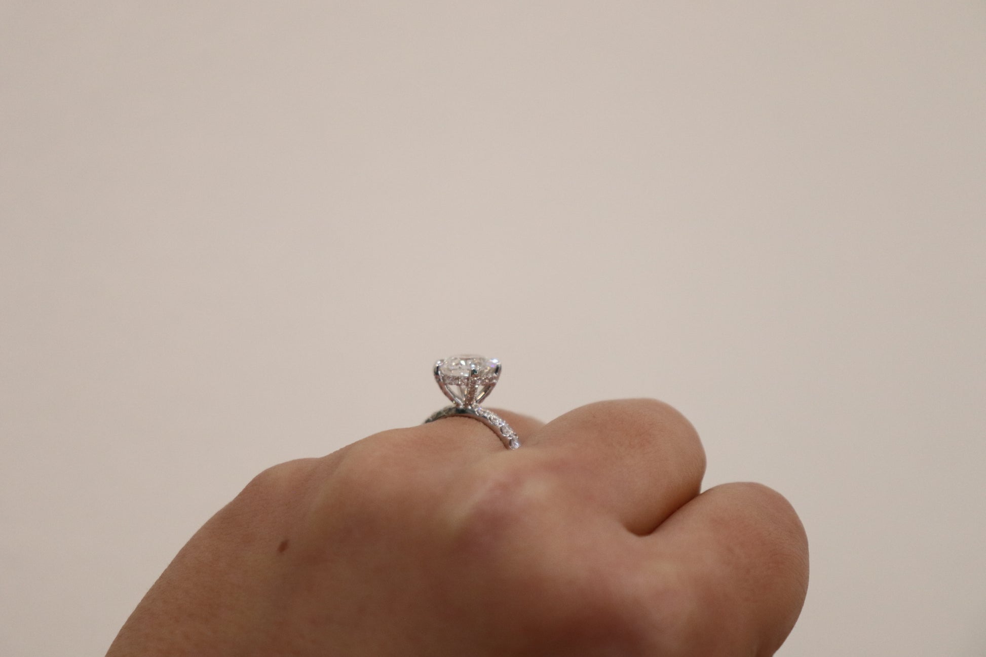 Hand wearing a diamond ring on a plain background