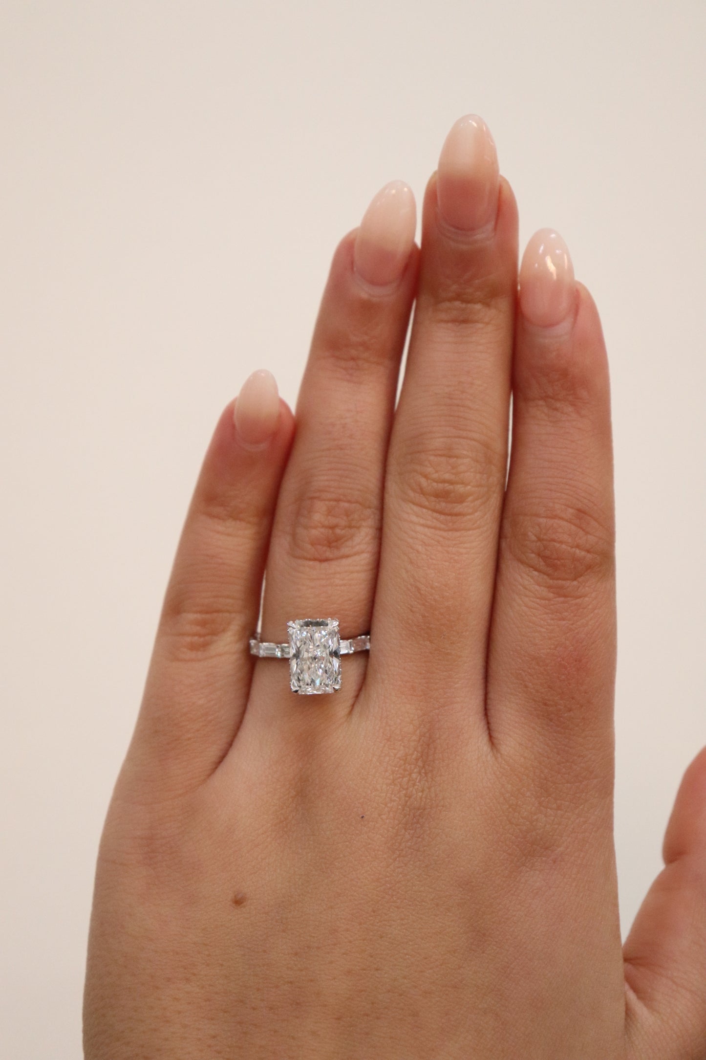 Radiant cut Diamond ring on a hand against a plain background