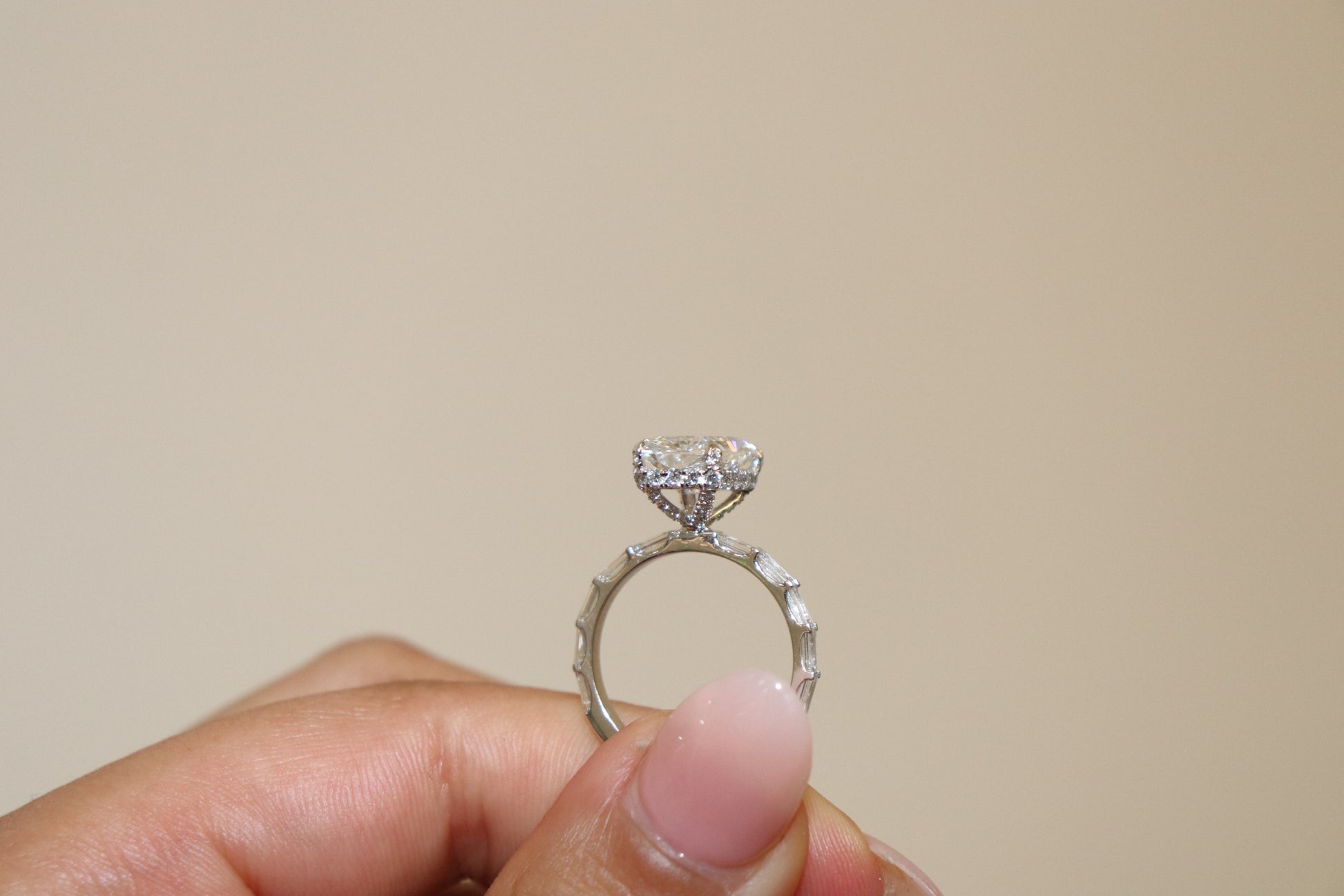 Radiant cut Diamond ring held in a hand against a beige background