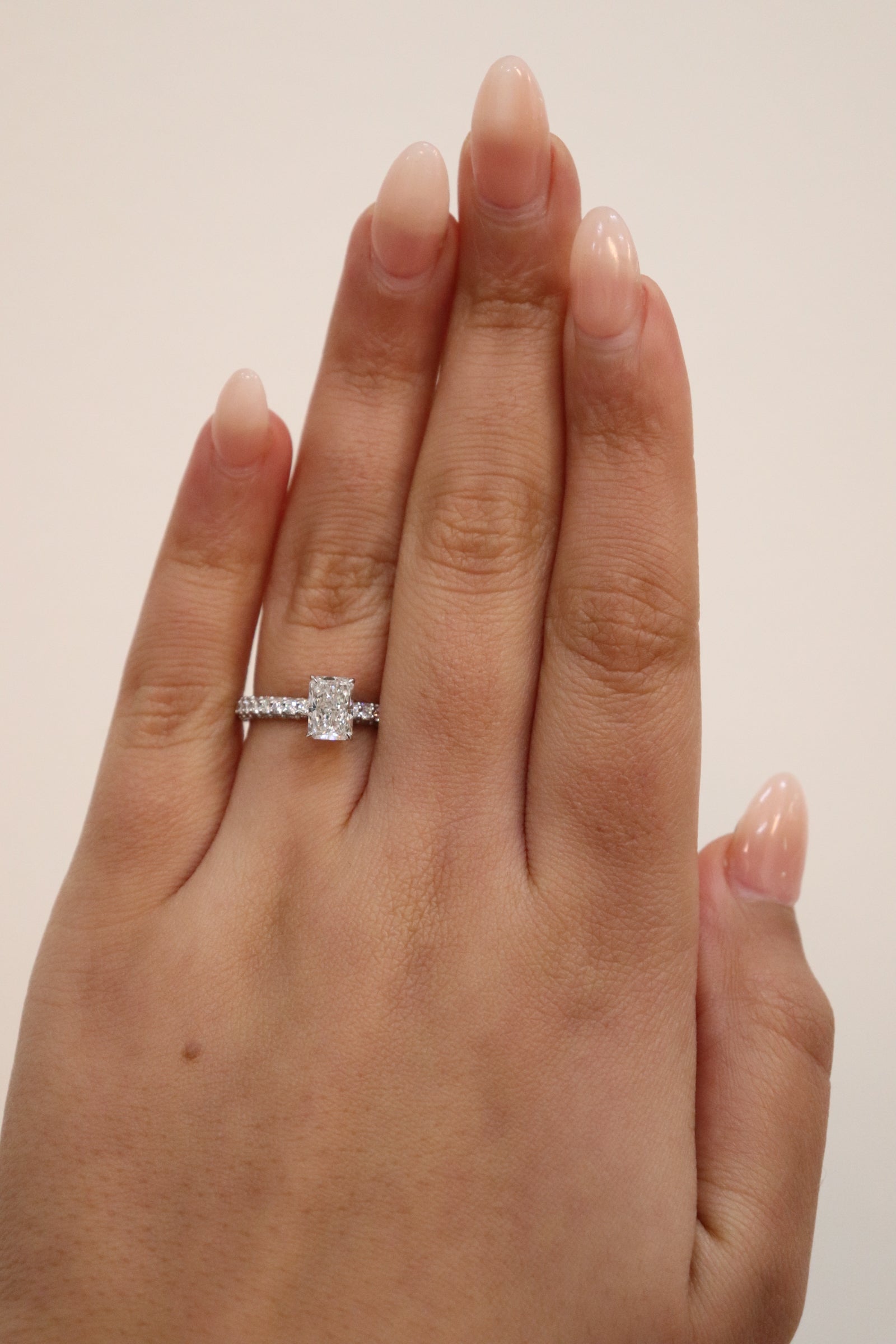 Hand wearing a radiant cut diamond ring with triple pavè band on a neutral background