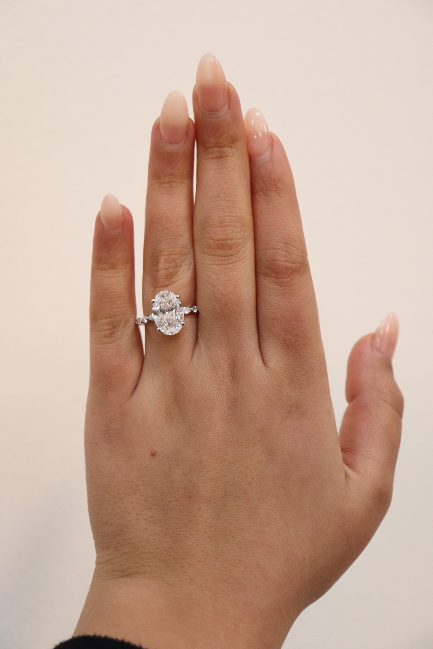 Hand wearing an Oval engagement ring with marquise and round accent band
