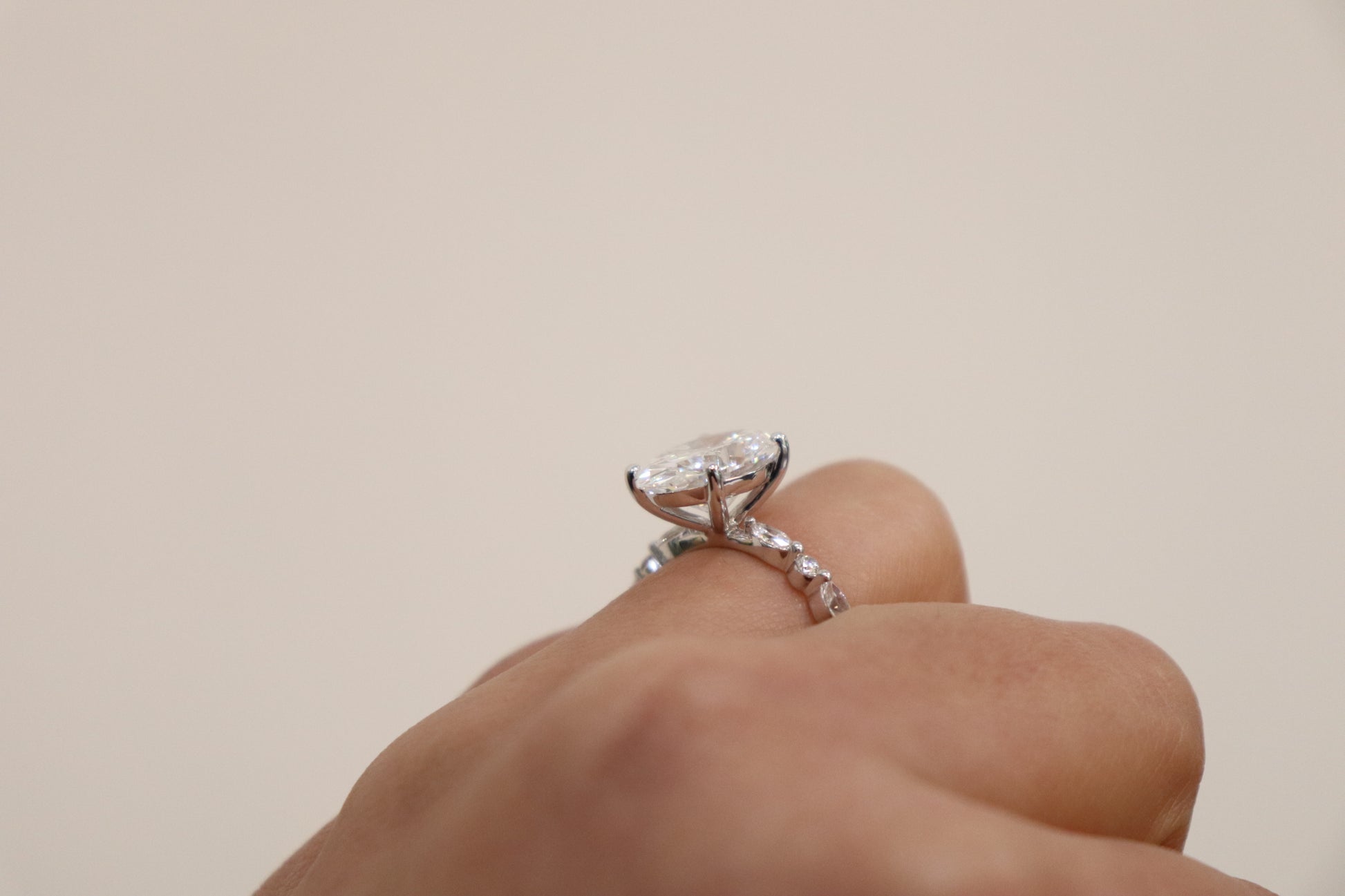 Hand wearing an Oval engagement ring with marquise and round accent band